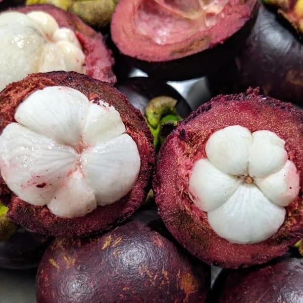 Close-up of several mangosteens, some whole and some cut open revealing white fruit segments.