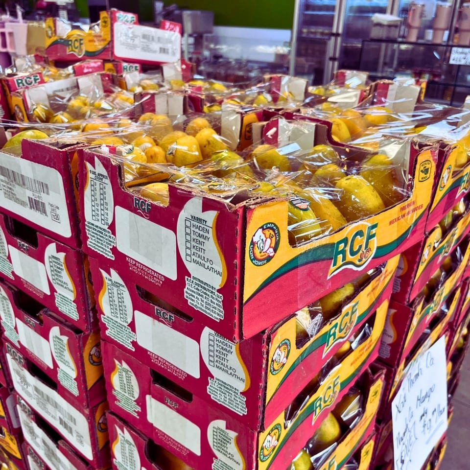 Stacked boxes of RCF premium Mexican mangoes, individually wrapped in plastic, at Linda's Tropical Fruits.